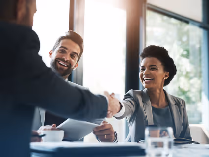Two business people shaking hands across a meeting table